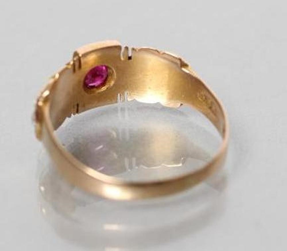 A LATE VICTORIAN 15CT GOLD RING centred by a gypsy set ruby within panelled shoulders each set with Image