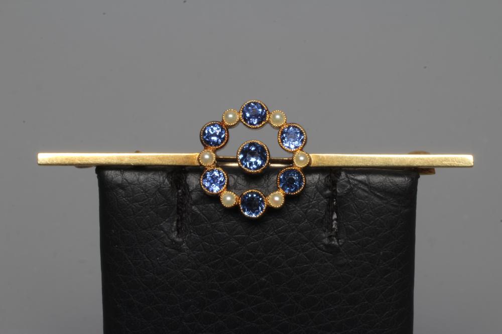 AN EDWARDIAN BAR BROOCH centred by a circular facet cut sapphire within an open border of six collet Image