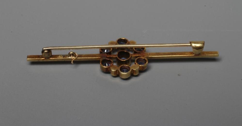 AN EDWARDIAN BAR BROOCH centred by a circular facet cut sapphire within an open border of six collet Image