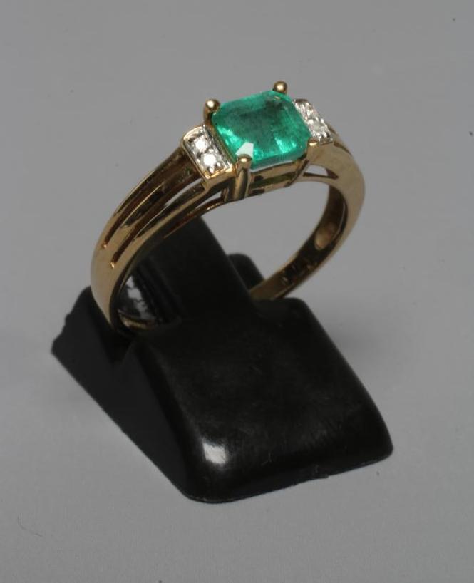 AN EMERALD RING, the oblong facet cut stone claw set between shoulders each pave set with two Image