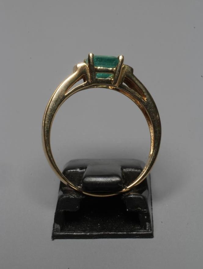 AN EMERALD RING, the oblong facet cut stone claw set between shoulders each pave set with two Image