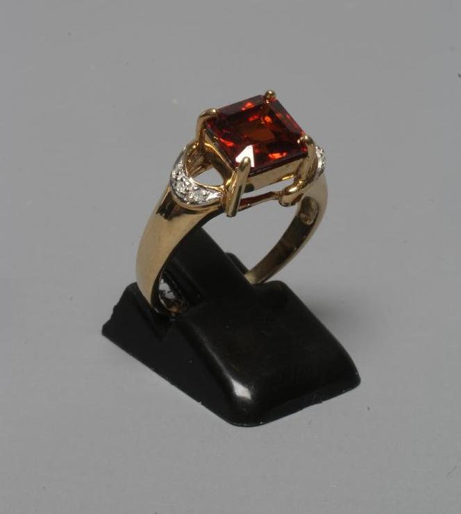 A DRESS RING, the claw set square cut garnet between open horseshoe shoulders each pave set with Image