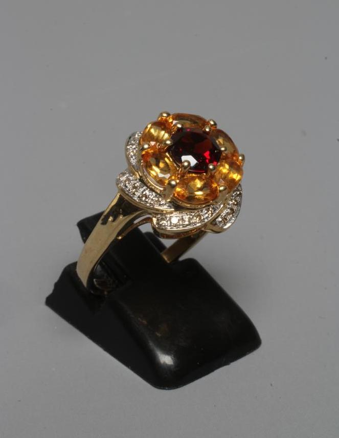 A MULTI-GEM COCKTAIL RING centred by a circular facet cut garnet within a border of six oval facet Image