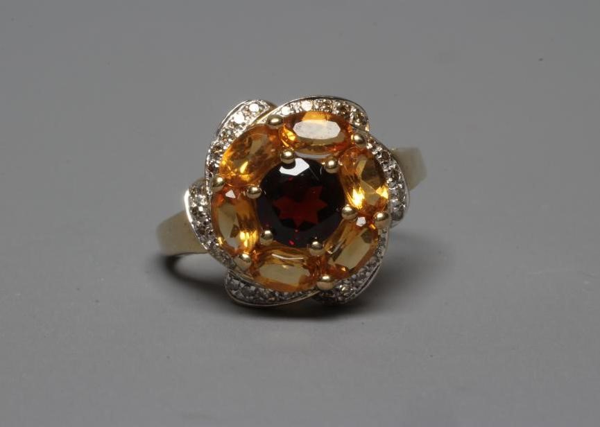 A MULTI-GEM COCKTAIL RING centred by a circular facet cut garnet within a border of six oval facet Image