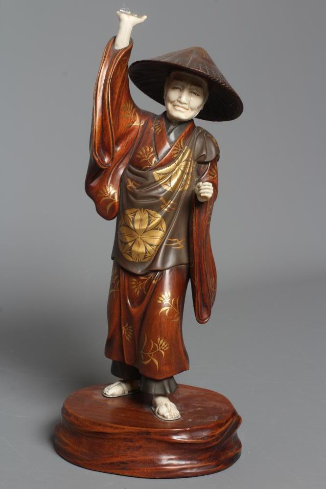 A JAPANESE CARVED WOOD AND IVORY OKIMONO modelled as a man wearing a kasa and gold highlighted Image