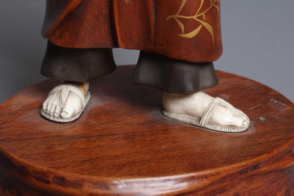 A JAPANESE CARVED WOOD AND IVORY OKIMONO modelled as a man wearing a kasa and gold highlighted Image