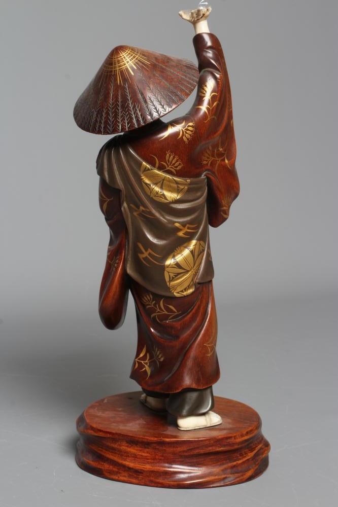 A JAPANESE CARVED WOOD AND IVORY OKIMONO modelled as a man wearing a kasa and gold highlighted Image