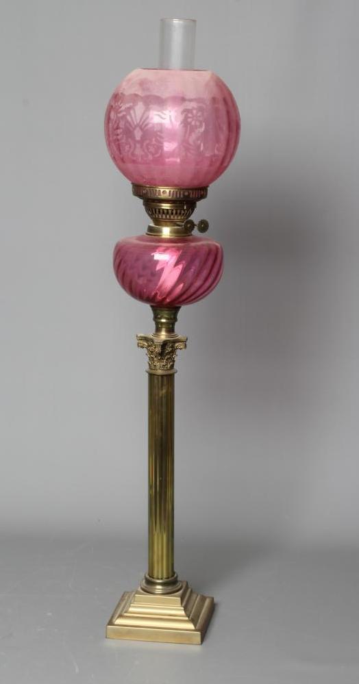 A VICTORIAN BRASS CORINTHIAN COLUMN OIL LAMP with etched cranberry spherical shade and clear chimney Image