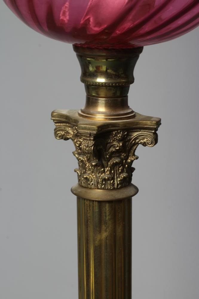 A VICTORIAN BRASS CORINTHIAN COLUMN OIL LAMP with etched cranberry spherical shade and clear chimney Image