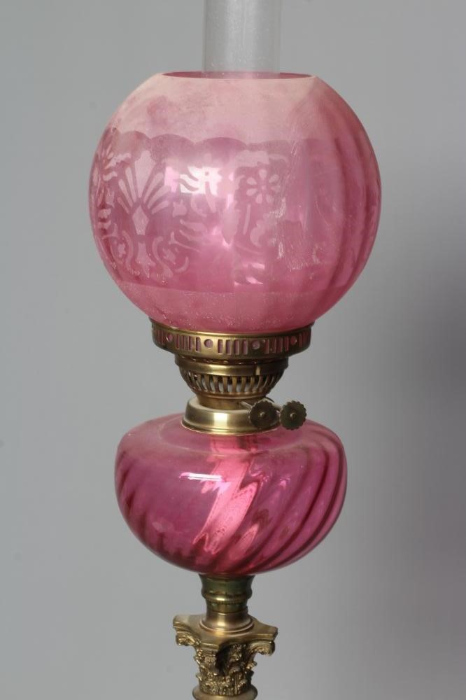 A VICTORIAN BRASS CORINTHIAN COLUMN OIL LAMP with etched cranberry spherical shade and clear chimney Image