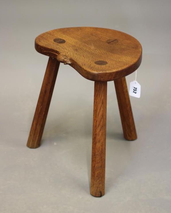 A ROBERT THOMPSON OAK COW STOOL, the kidney shaped seat raised on three splayed faceted legs, carved Image
