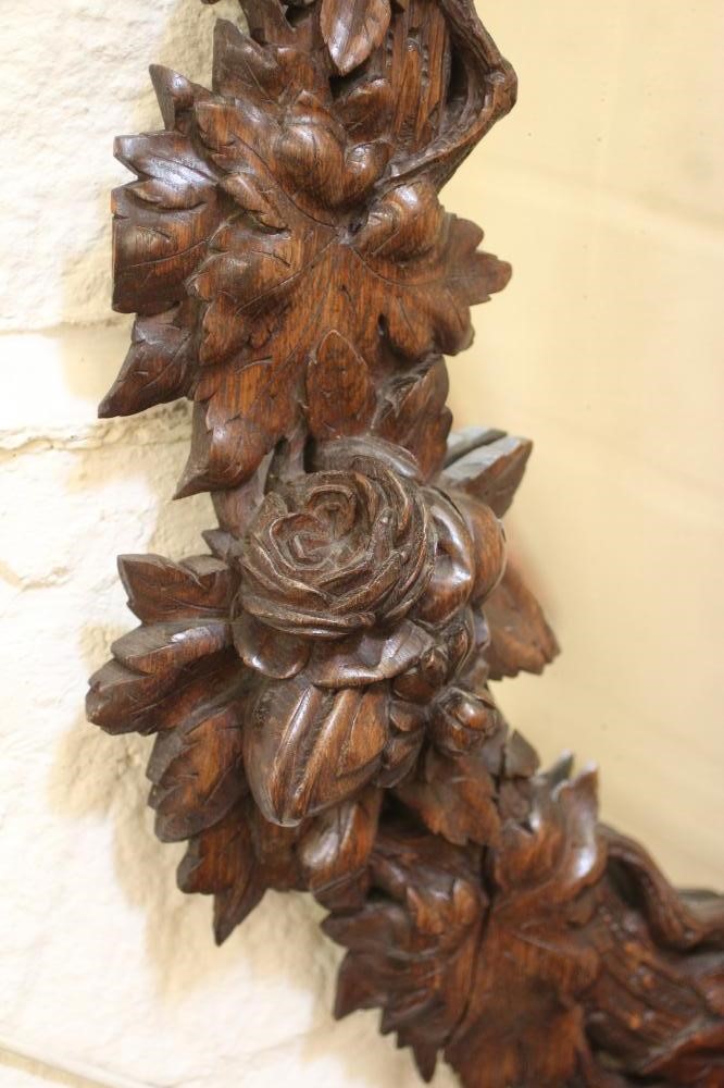 A CARVED OAK PIER GLASS, c.1900, the oval plate within a boldly carved frame with flowers and Image