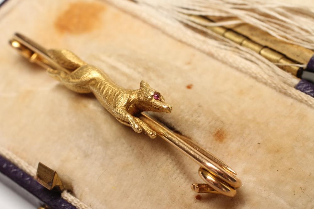 A NOVELTY STOCK BROOCH centred by a fox in flight with a ruby cabochon eye Image