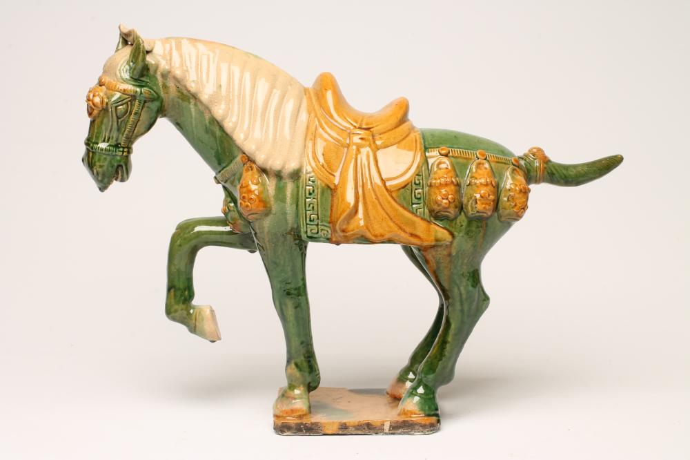 A TANG STYLE EARTHENWARE HORSE standing with right fore-leg raised and with saddle and bridle Image