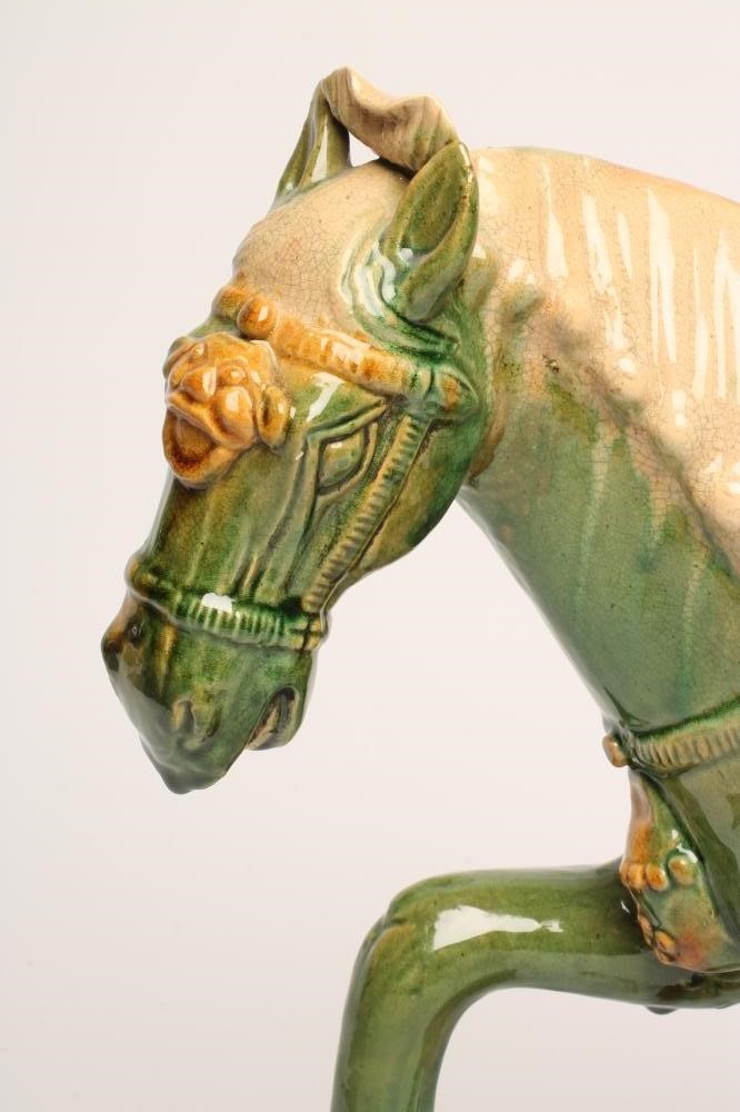 A TANG STYLE EARTHENWARE HORSE standing with right fore-leg raised and with saddle and bridle Image