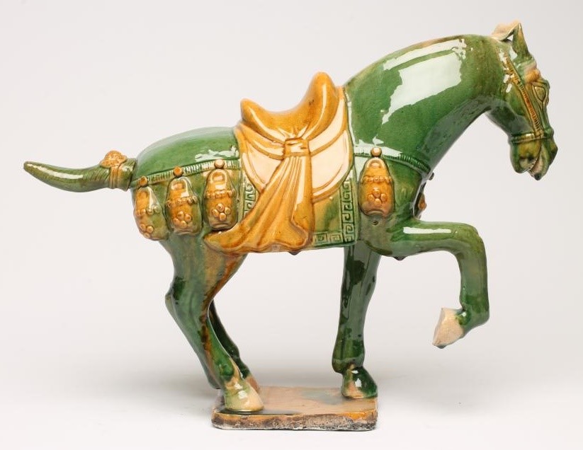 A TANG STYLE EARTHENWARE HORSE standing with right fore-leg raised and with saddle and bridle Image