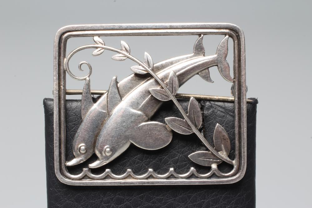 A GEORG JENSEN SILVER OBLONG BROOCH designed by Arno Malinowski cast as two dolphins swimming amidst Image