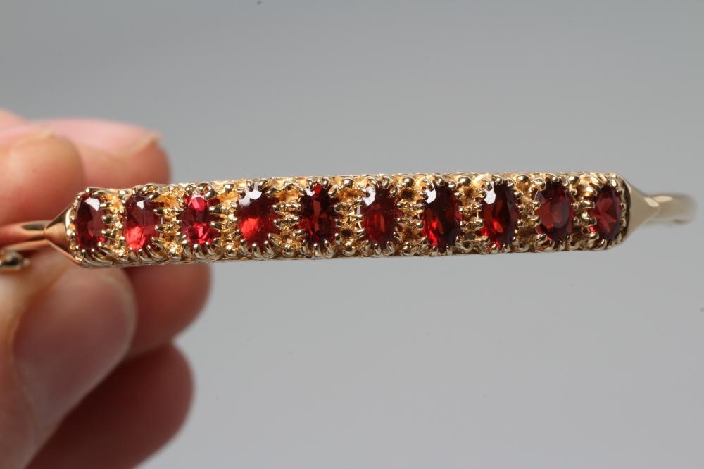 A STIFF HINGED BANGLE, the upper section claw set with ten oval facet cut garnets, indistinctly Image