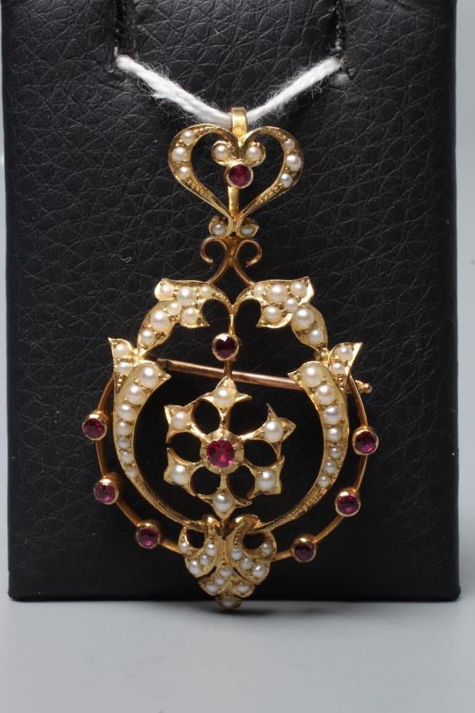 AN EDWARDIAN RUBY AND SEED PEARL PENDANT/BROOCH of shaped open oval form centred by a flowerhead and Image
