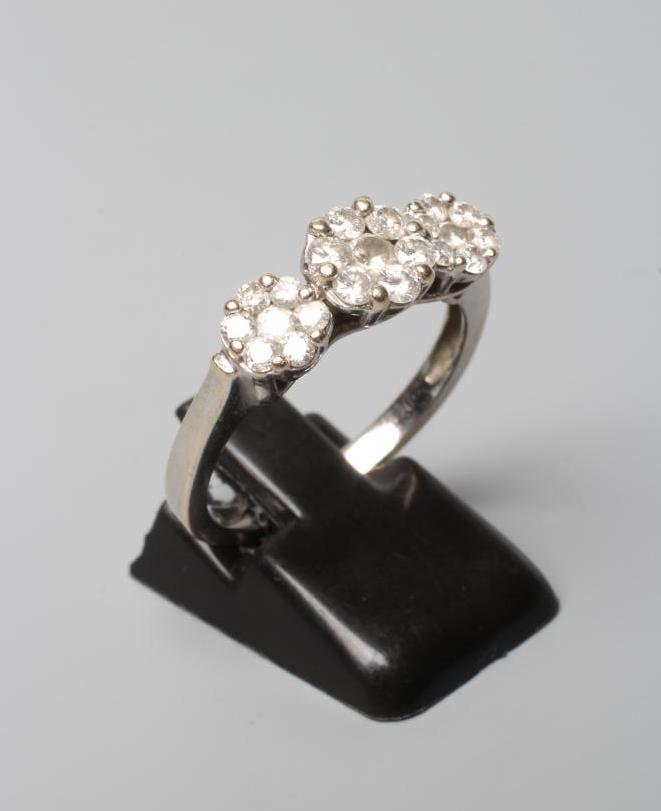 A DIAMOND TRIPLE CLUSTER RING, the graduated seven stone clusters claw set to a plain shank stamped Image
