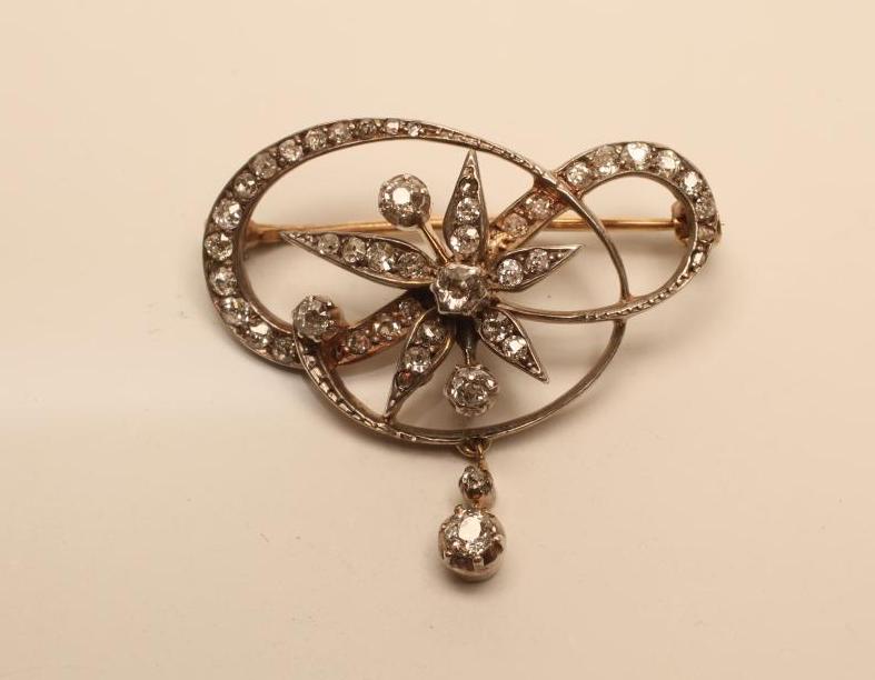 A VICTORIAN DIAMOND BROOCH of open scroll form centred by a stylised flowerhead and with diamond Image
