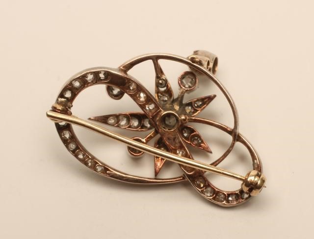 A VICTORIAN DIAMOND BROOCH of open scroll form centred by a stylised flowerhead and with diamond Image