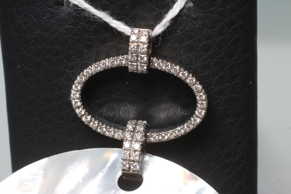 A MOTHER OF PEARL POLISHED CIRCULAR PENDANT hung from a diamond set open oval panel on similar set Image
