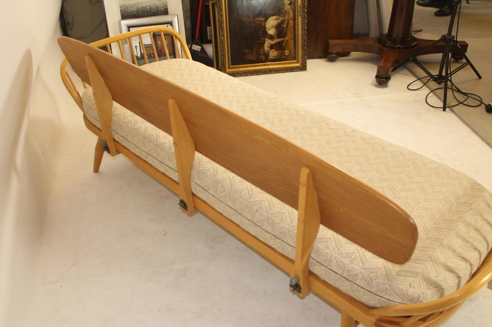 AN ERCOL BEECH AND ELM STUDIO COUCH of rounded oblong form with raised solid back and hooped ends on Image