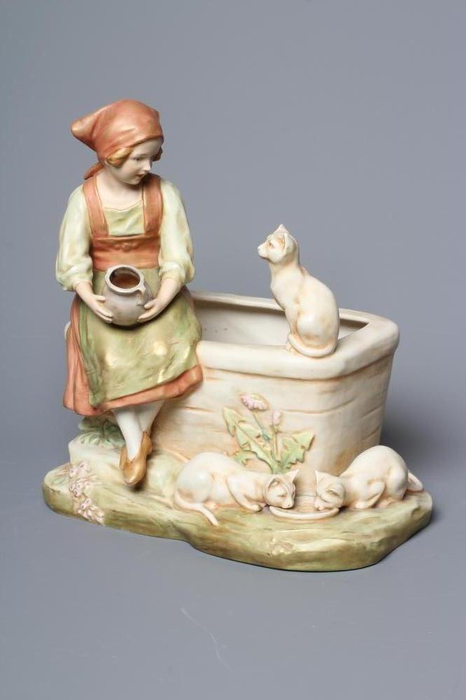 AN ART NOUVEAU ROYAL DUX FIGURE modelled as a young girl in traditional garb seated on the side of a Image