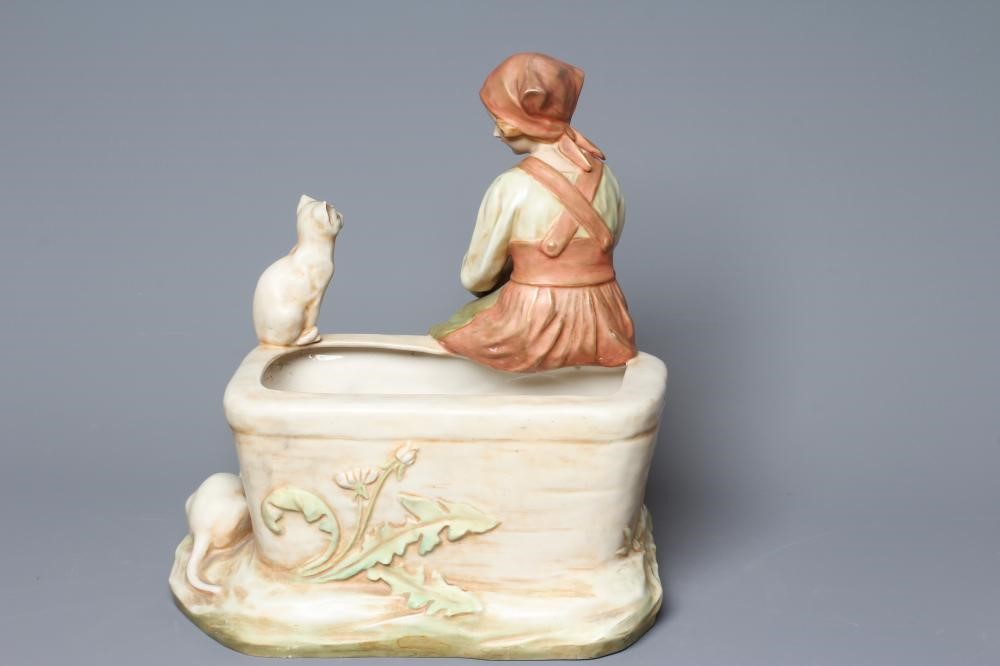 AN ART NOUVEAU ROYAL DUX FIGURE modelled as a young girl in traditional garb seated on the side of a Image