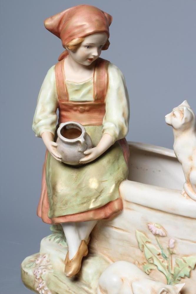 AN ART NOUVEAU ROYAL DUX FIGURE modelled as a young girl in traditional garb seated on the side of a Image