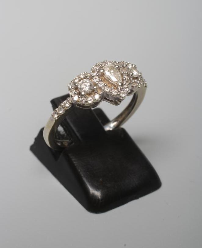 A DIAMOND RING, the central pear cut stone claw set to an oval border of small brilliant cut stones Image
