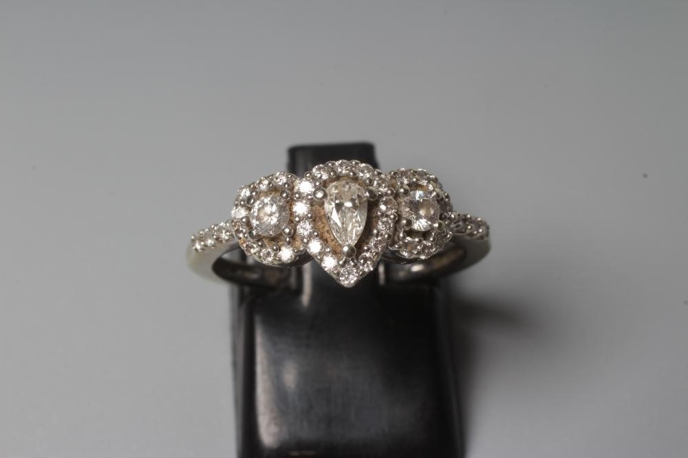 A DIAMOND RING, the central pear cut stone claw set to an oval border of small brilliant cut stones Image