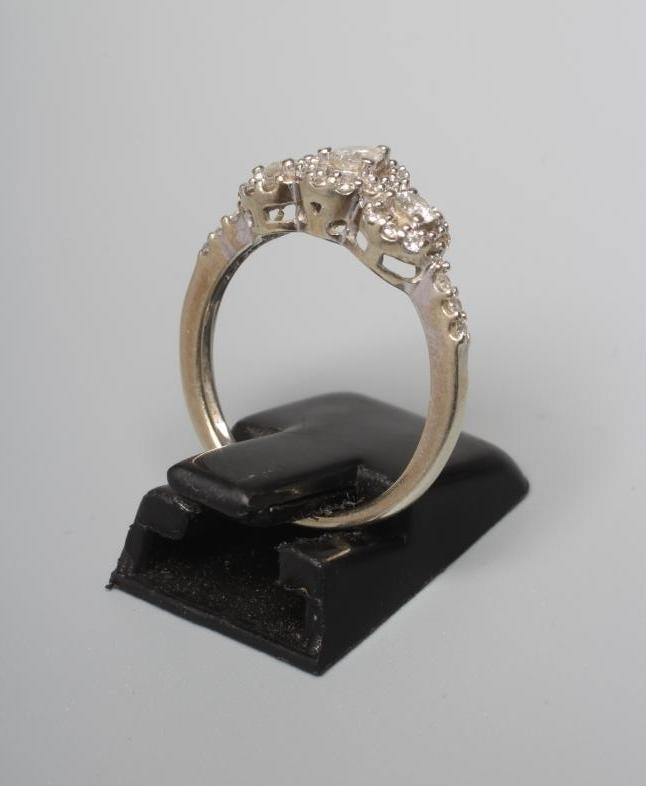 A DIAMOND RING, the central pear cut stone claw set to an oval border of small brilliant cut stones Image