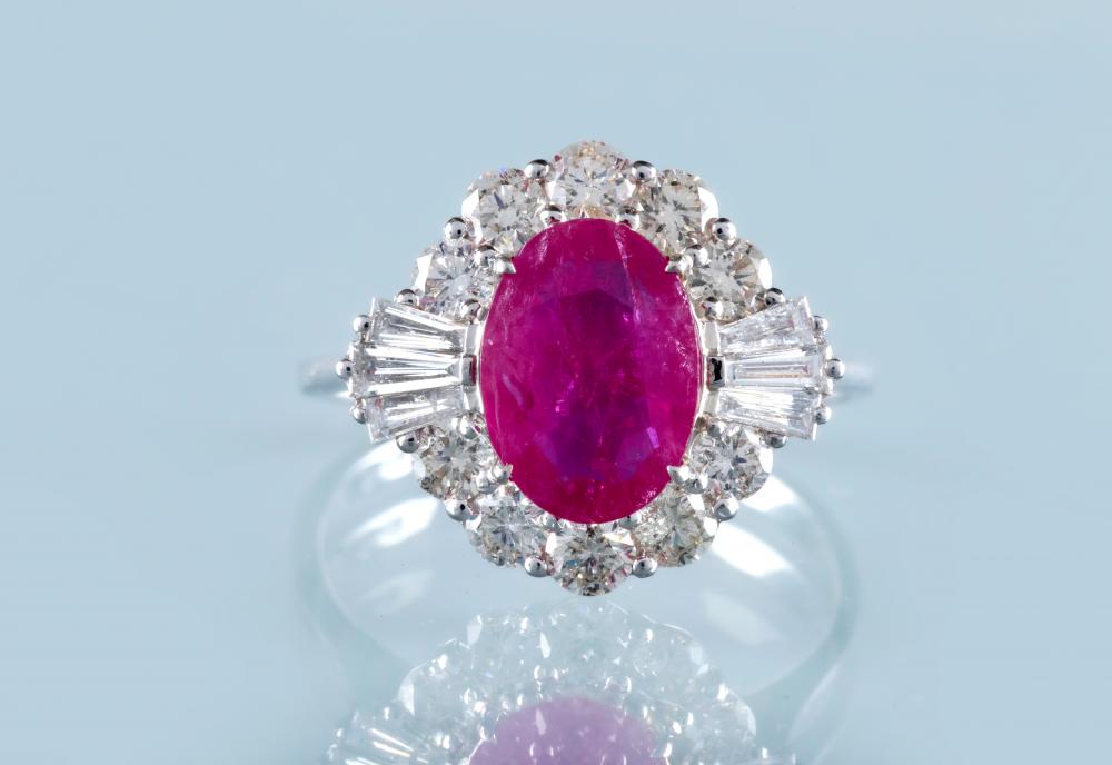 A RUBY AND DIAMOND CLUSTER RING, the oval facet cut ruby claw set to a border of ten round brilliant Image