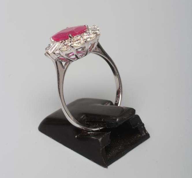 A RUBY AND DIAMOND CLUSTER RING, the oval facet cut ruby claw set to a border of ten round brilliant Image
