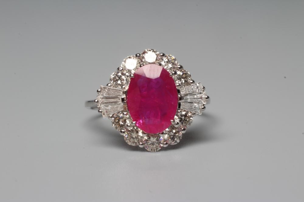 A RUBY AND DIAMOND CLUSTER RING, the oval facet cut ruby claw set to a border of ten round brilliant Image