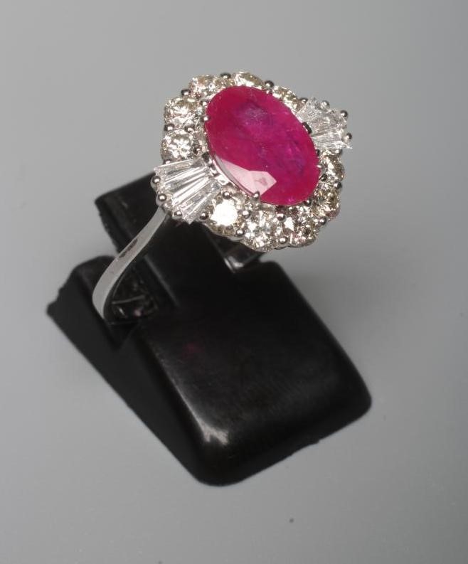 A RUBY AND DIAMOND CLUSTER RING, the oval facet cut ruby claw set to a border of ten round brilliant Image