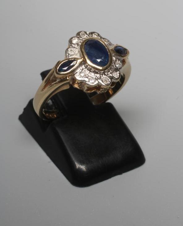 A SAPPHIRE AND DIAMOND CLUSTER RING, the central oval facet cut sapphire in rub over setting within Image