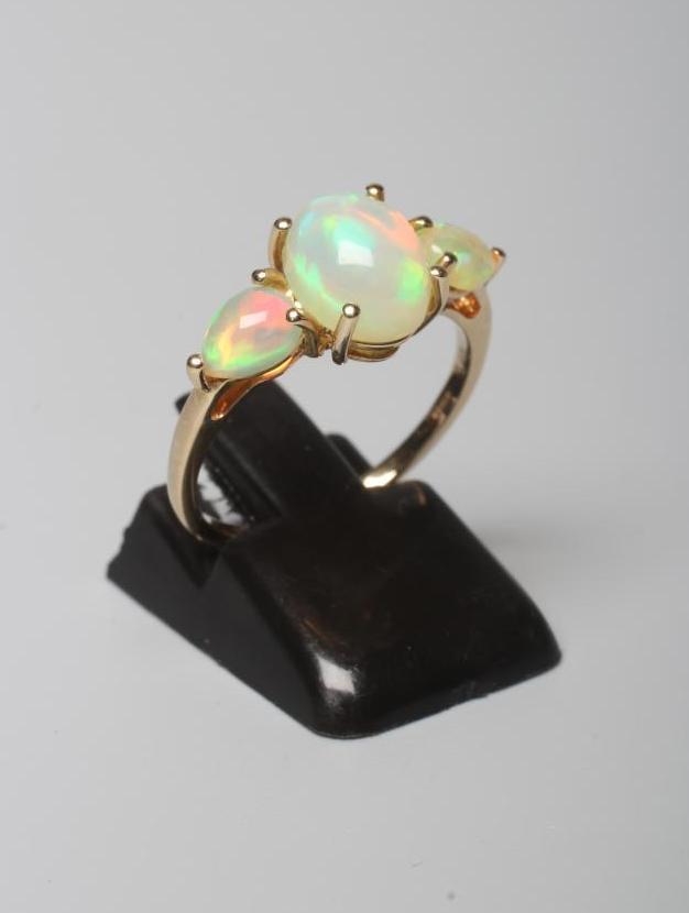 AN OPAL DRESS RING, the central oval cabochon polished stone vertically claw set and flanked by two Image