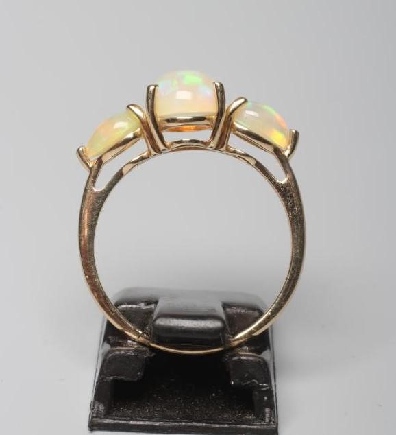 AN OPAL DRESS RING, the central oval cabochon polished stone vertically claw set and flanked by two Image