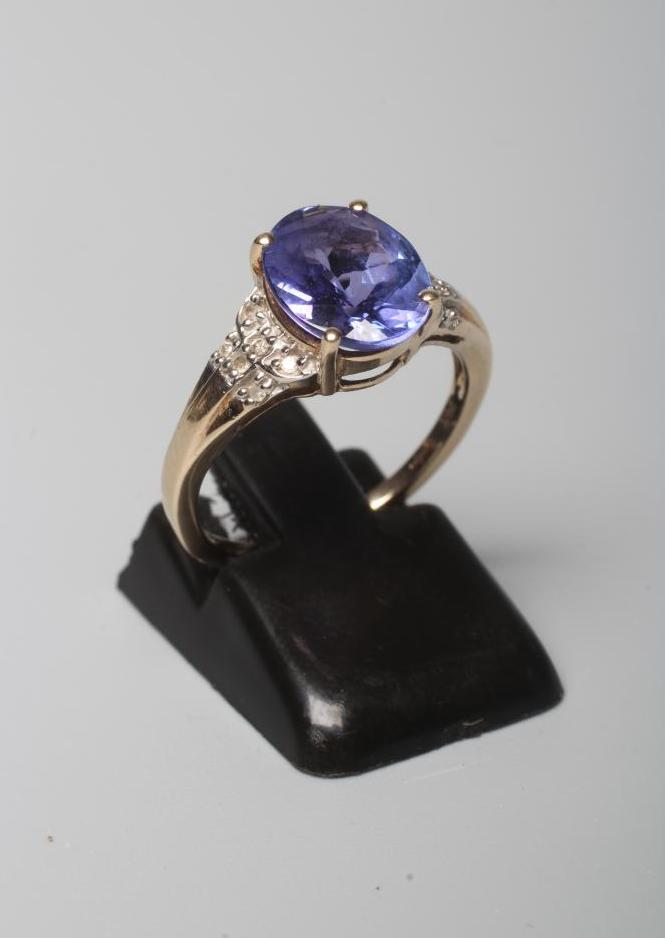 A TANZANITE DRESS RING, the oval facet cut stone claw set to reeded shoulders each pave set with six Image