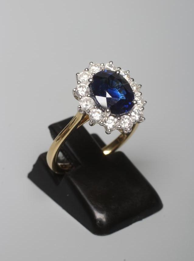A SAPPHIRE AND DIAMOND CLUSTER RING, the oval facet cut sapphire of 3.03cts claw set to a border of Image