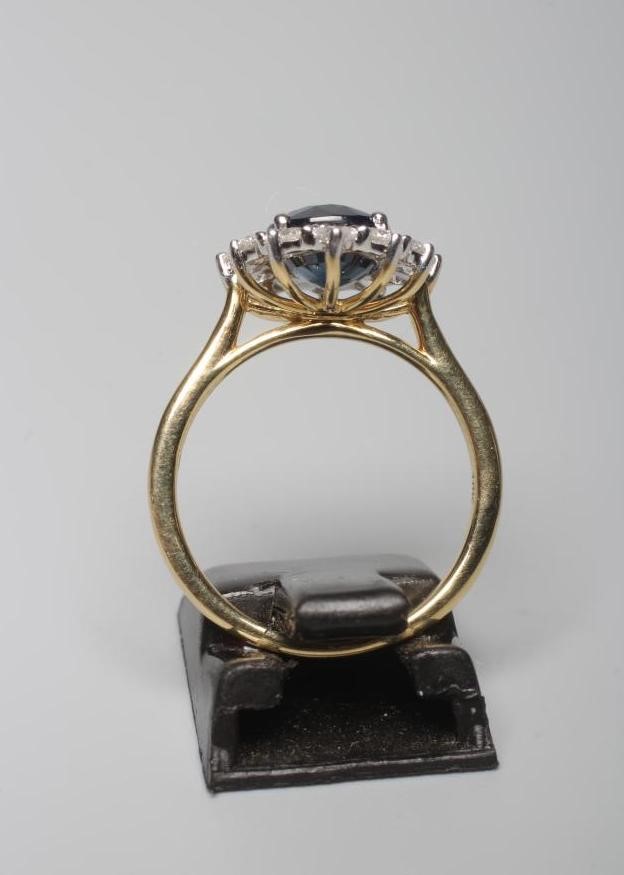 A SAPPHIRE AND DIAMOND CLUSTER RING, the oval facet cut sapphire of 3.03cts claw set to a border of Image