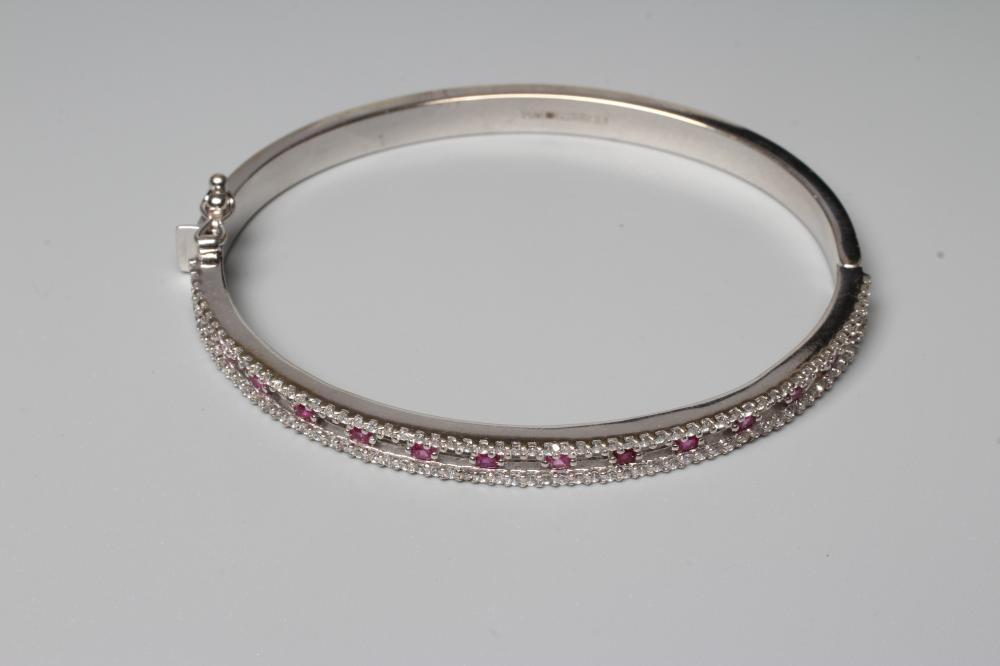 A RUBY AND DIAMOND STIFF HINGED BANGLE, the open upper section claw set with fourteen small rubies Image
