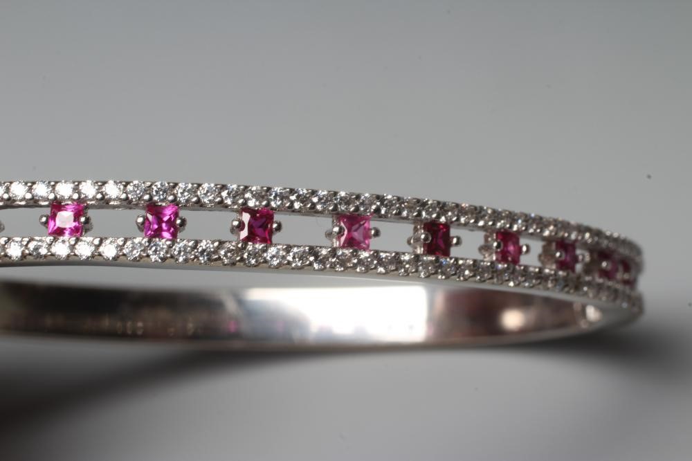 A RUBY AND DIAMOND STIFF HINGED BANGLE, the open upper section claw set with fourteen small rubies Image