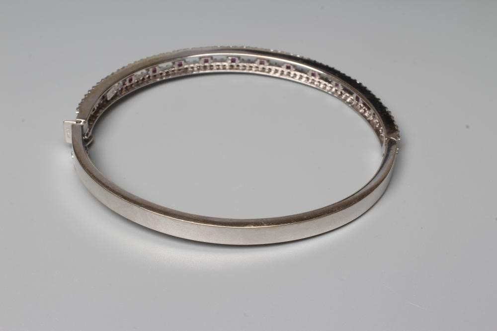 A RUBY AND DIAMOND STIFF HINGED BANGLE, the open upper section claw set with fourteen small rubies Image