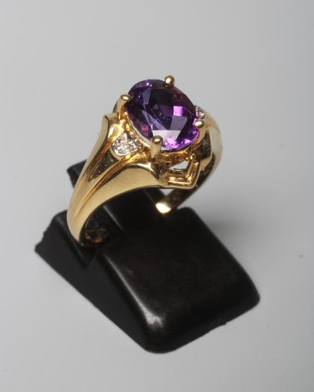 AN AMETHYST RING, the oval facet cut stone claw set to wide shaped shoulders each point set with a Image