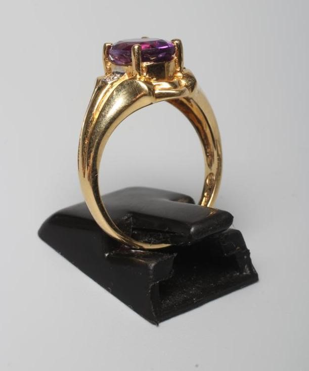 AN AMETHYST RING, the oval facet cut stone claw set to wide shaped shoulders each point set with a Image
