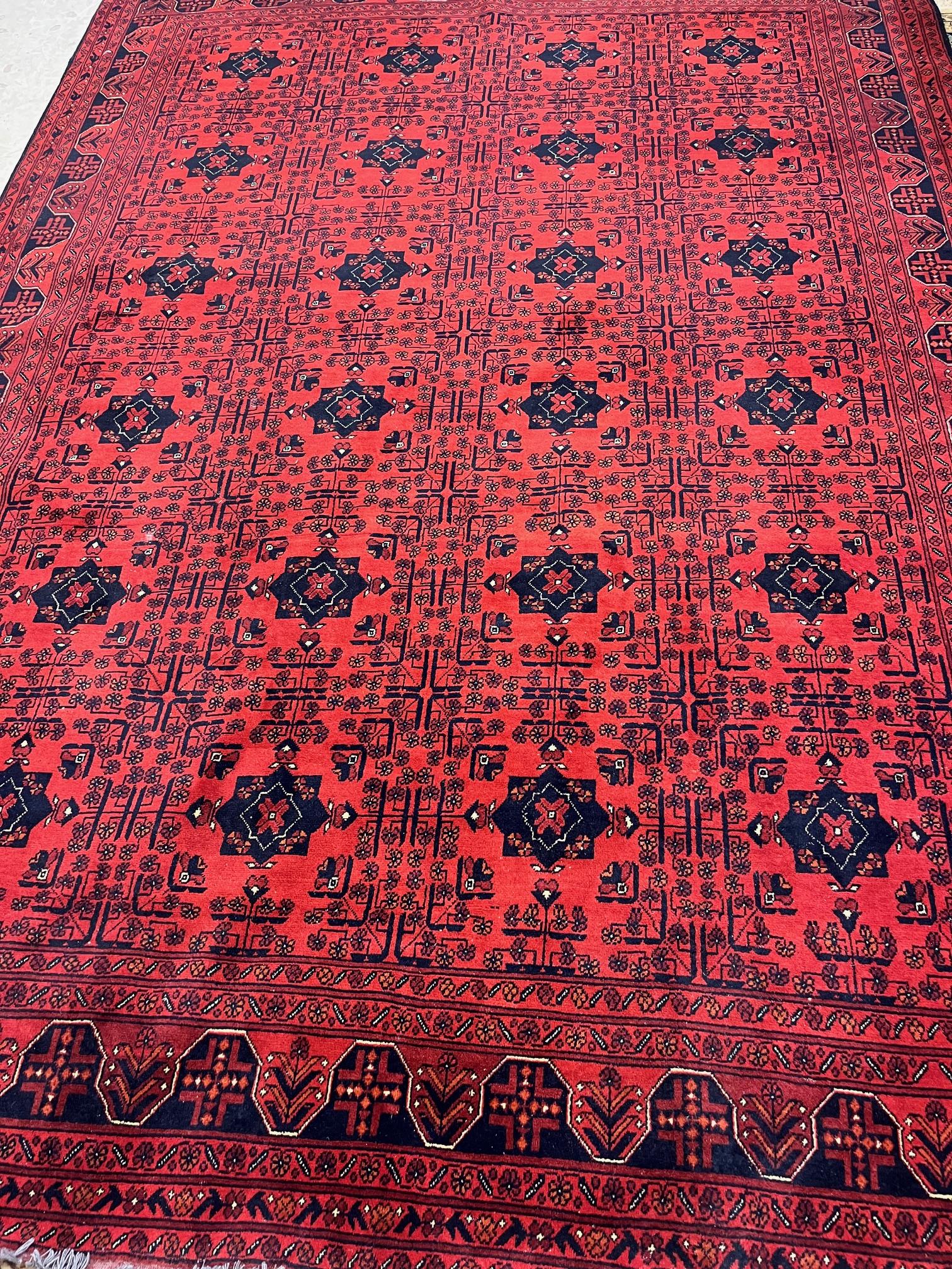 AN AFGHAN WOOL FRINGED CARPET, modern, the red ground with repeating navy blue gul pattern, 11' 2" x Image